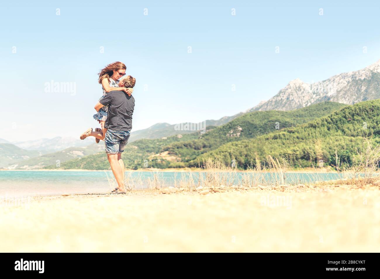 Hombre levantando a la mujer en el aire. Feliz pareja riendo de vacaciones. Paisaje de montaña. Novio llevando novia. Momento romántico después de la propuesta. Foto de stock