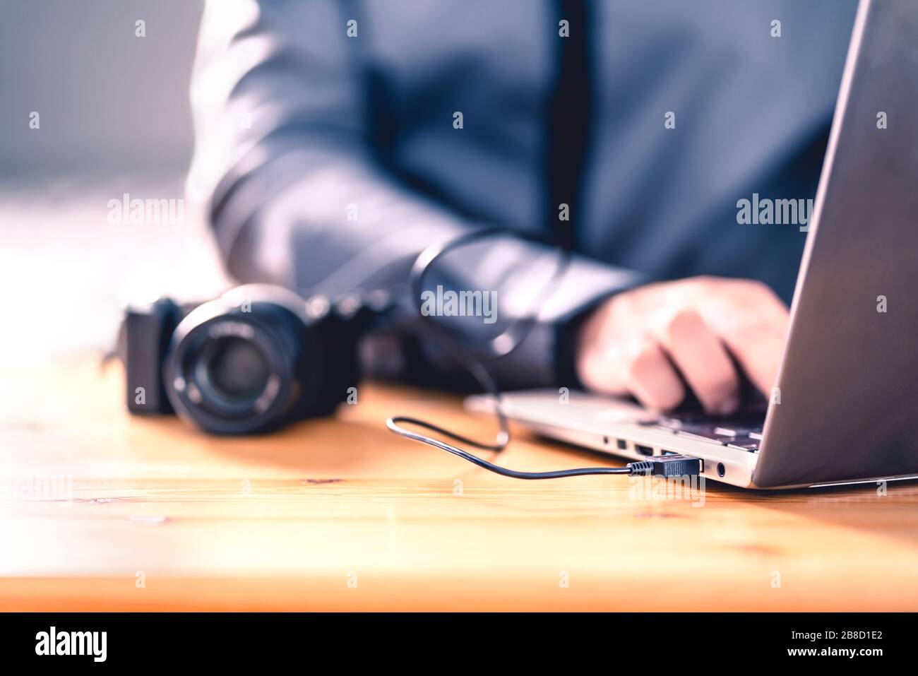 Cámara conectada al portátil con cable usb. Hombre editando fotos con software informático. El fotógrafo transfiere archivos al ordenador desde una cámara réflex digital. Foto de stock