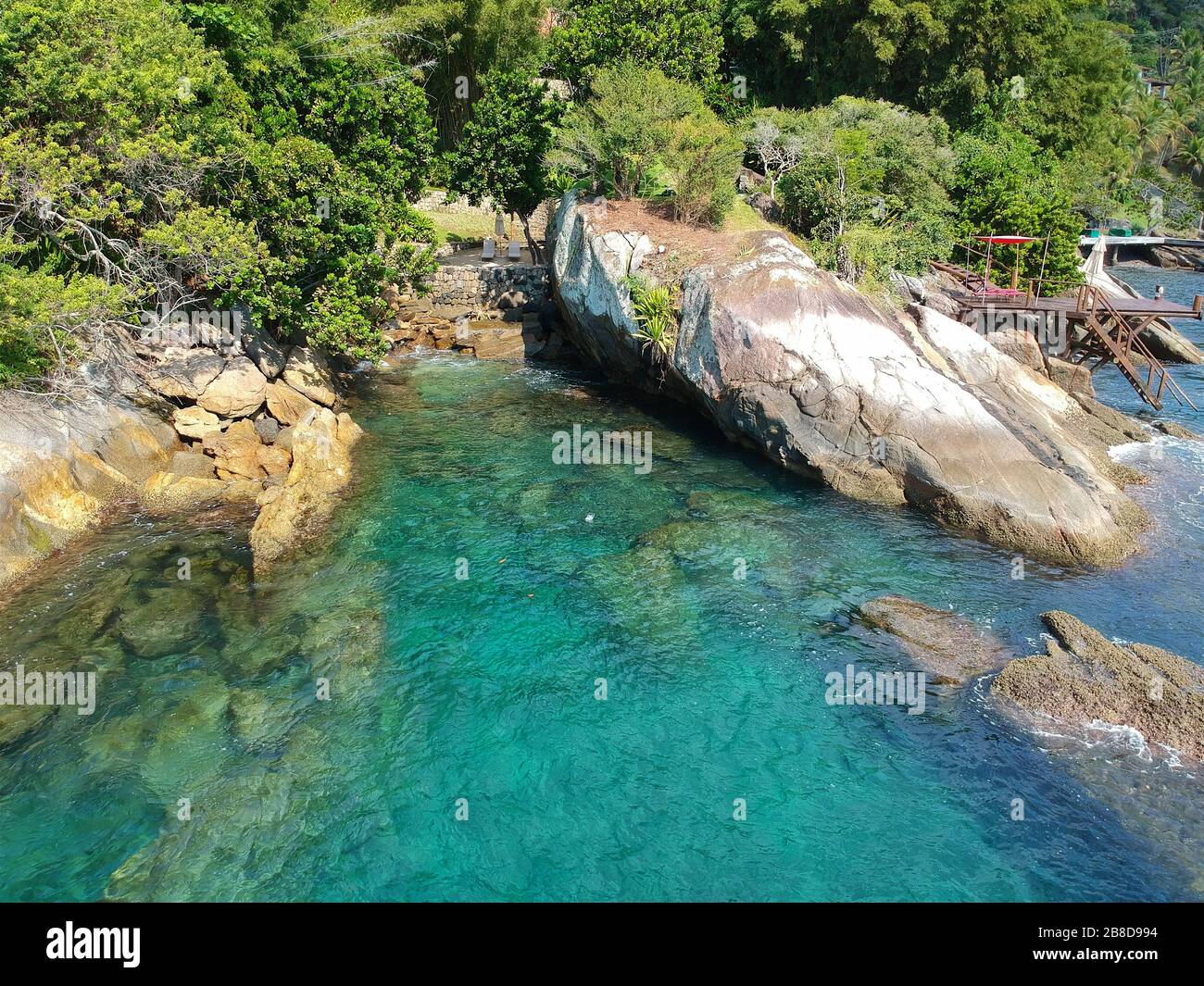 Vista aérea de un pequeño y tranquilo jardín con sillas de madera entre rocas y junto al océano aguas cristalinas en el país tropical. Brasil Foto de stock