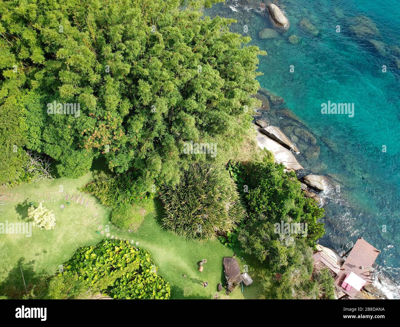 Vista aérea de un pequeño y tranquilo jardín con sillas de madera entre rocas y junto al océano aguas cristalinas en el país tropical. Brasil Foto de stock