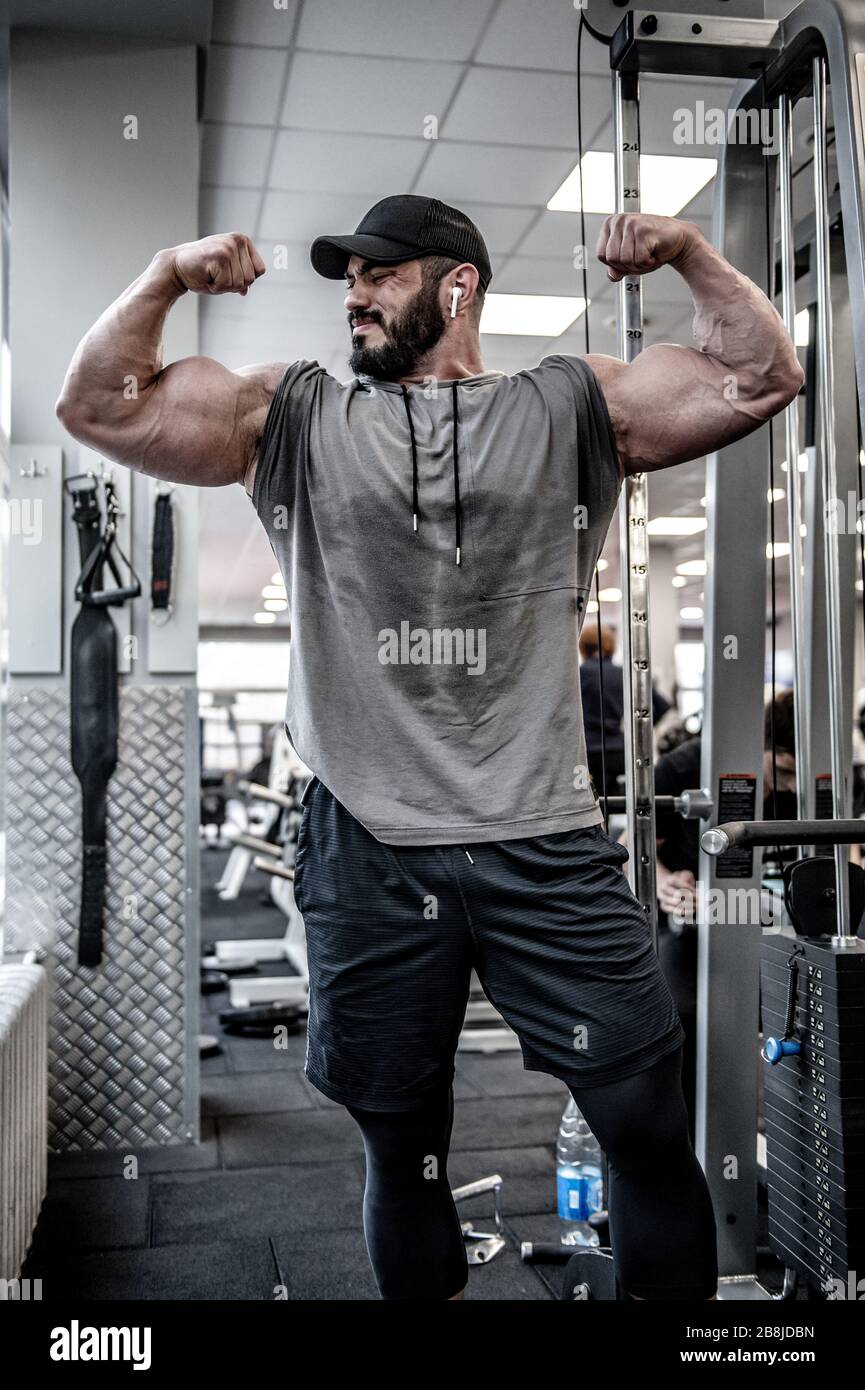 Forte jovem atleta homem com barba vestindo top tanque preto mostrando  grande músculo duplo bíceps no ginásio esporte com janela fotos, imagens de  © photo_zaur.mail.ru #417425926