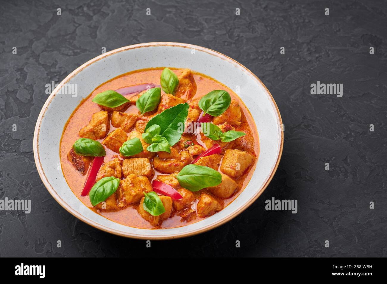 Curry de pollo al panang tailandés en placa blanca con fondo de pizarra negra. Phanaeng Curry es un plato de cocina tailandesa con pollo, hojas de lima kaffir y curry rojo sa Foto de stock