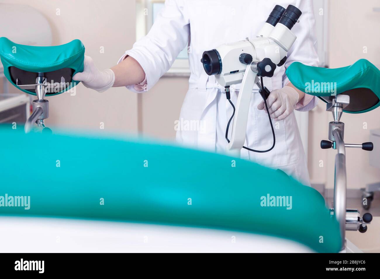 Sala ginecológica con silla y equipo. Manos de la doctora con herramientas para el examen de la salud de la mujer. Foto de stock