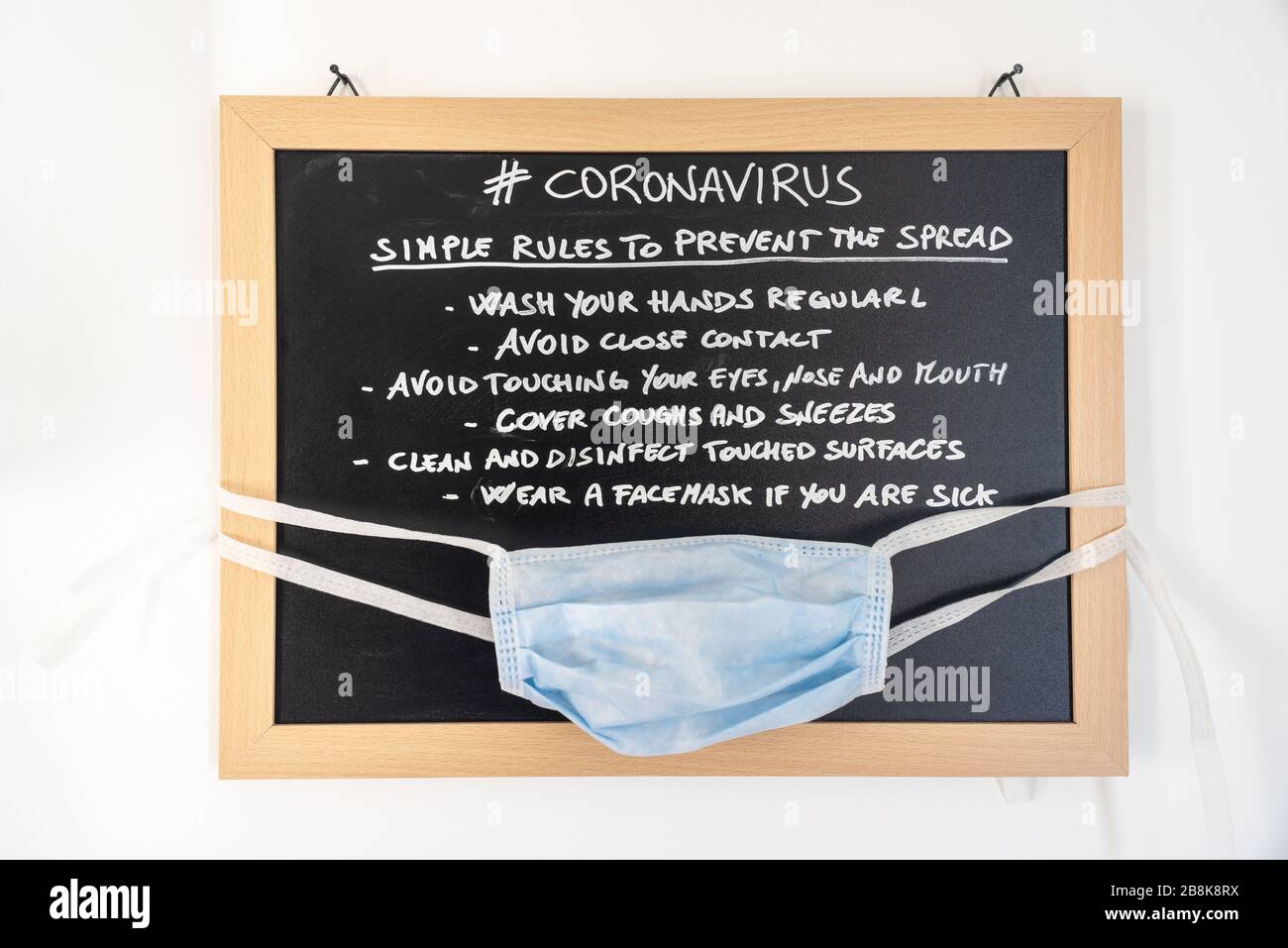 Pizarra con las reglas para evitar la propagación del coronavirus con una máscara segura colgada. Foto de stock