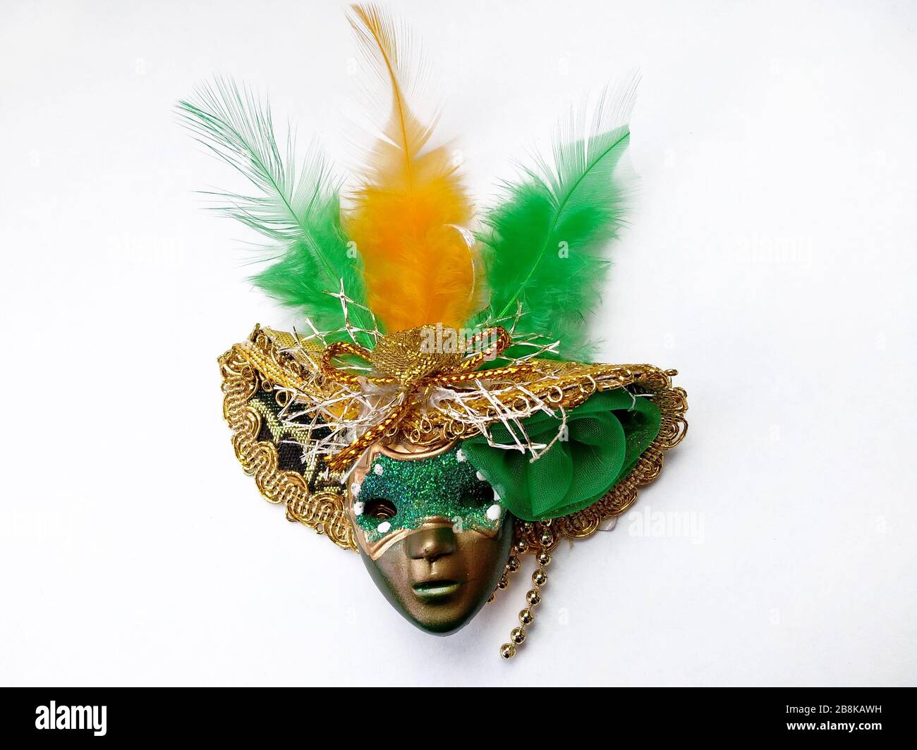 máscara de plástico en un sombrero con plumas en un fondo blanco vista  superior. Máscara verde en un sombrero con pluma verde y amarilla. Traje de  Carnaval f Fotografía de stock -