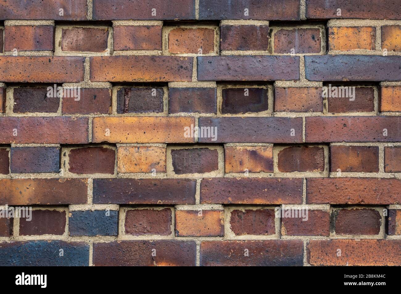 Pared del edificio hecha de ladrillos oscuros, amarillos a marrones del clinker con varios patrones alternantes. Las piedras son desplazadas en filas, giradas, indentadas o om Foto de stock