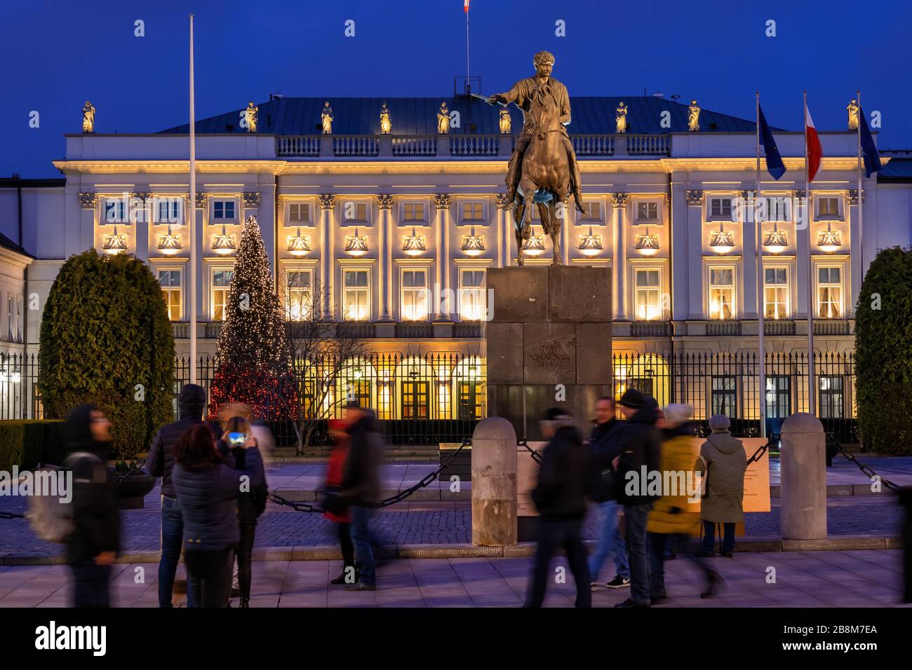 Varsovia, Polonia - 27 de diciembre de 2019: La gente en el Palacio Presidencial iluminado por la noche y Monumento al Príncipe Jozef Poniatowski, monumentos de la ciudad Foto de stock