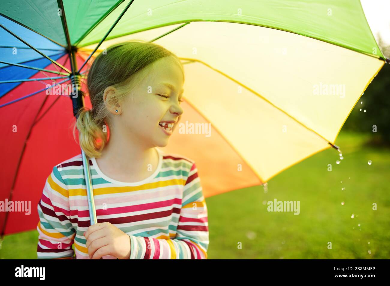 Sobretodo Inesperado radioactividad Linda chica joven sosteniendo un colorido paraguas arco iris el día  lluvioso de verano. Niño caminando bajo una lluvia cálida al aire libre.  Actividades al aire libre de verano para niños Fotografía