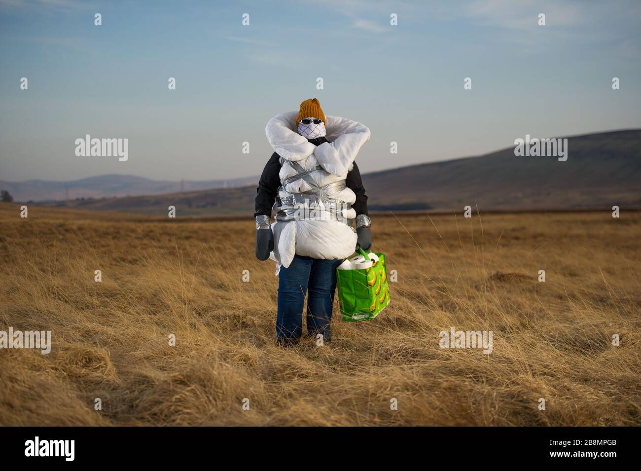 Perthshire Hills, Reino Unido. 22 de marzo de 2020. En la imagen: Imagen conceptual de una persona que va a longitudes extremas para auto aislar en el medio de la nada llevar el artículo más buscado en el mundo del papel higiénico, mientras que envuelto en el hogar hizo equipo de protección personal. Crédito: Colin Fisher/Alamy Live News Foto de stock