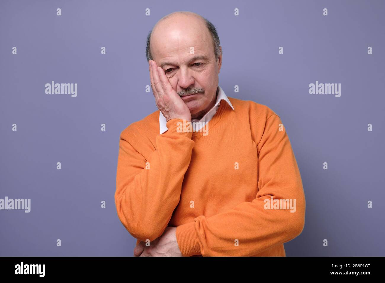 Triste y maduro hombre hispano en suéter de naranja sensación estresado y solo. Foto de stock
