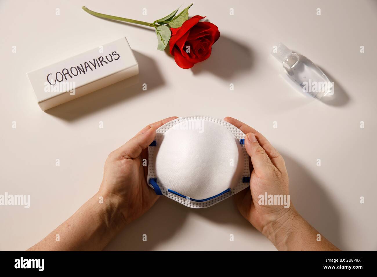 higiene de la salud del coronavirus o la lucha contra el concepto del coronavirus, manos que sostienen la máscara de protección personal, desinfectante de manos y rosa roja sobre la capa plana blanca, protéjase contra la pandemia del ataque del virus del covid 19 Foto de stock