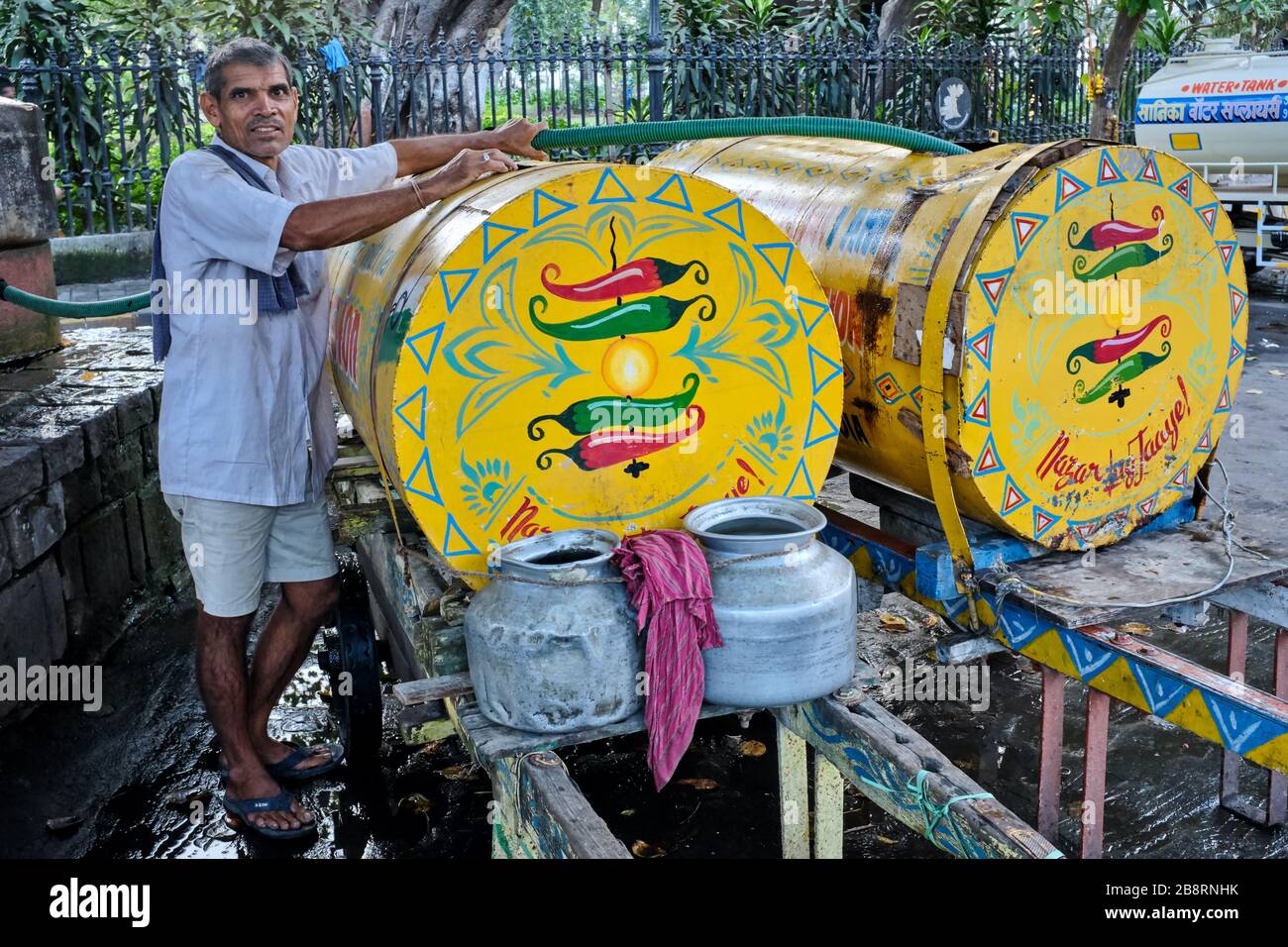 Un hombre que entrega agua llena su tanque de agua en un pozo en Horniman Circle.Mumbai, India, el agua que será entregada por el carro de mano a las oficinas en la zona Foto de stock