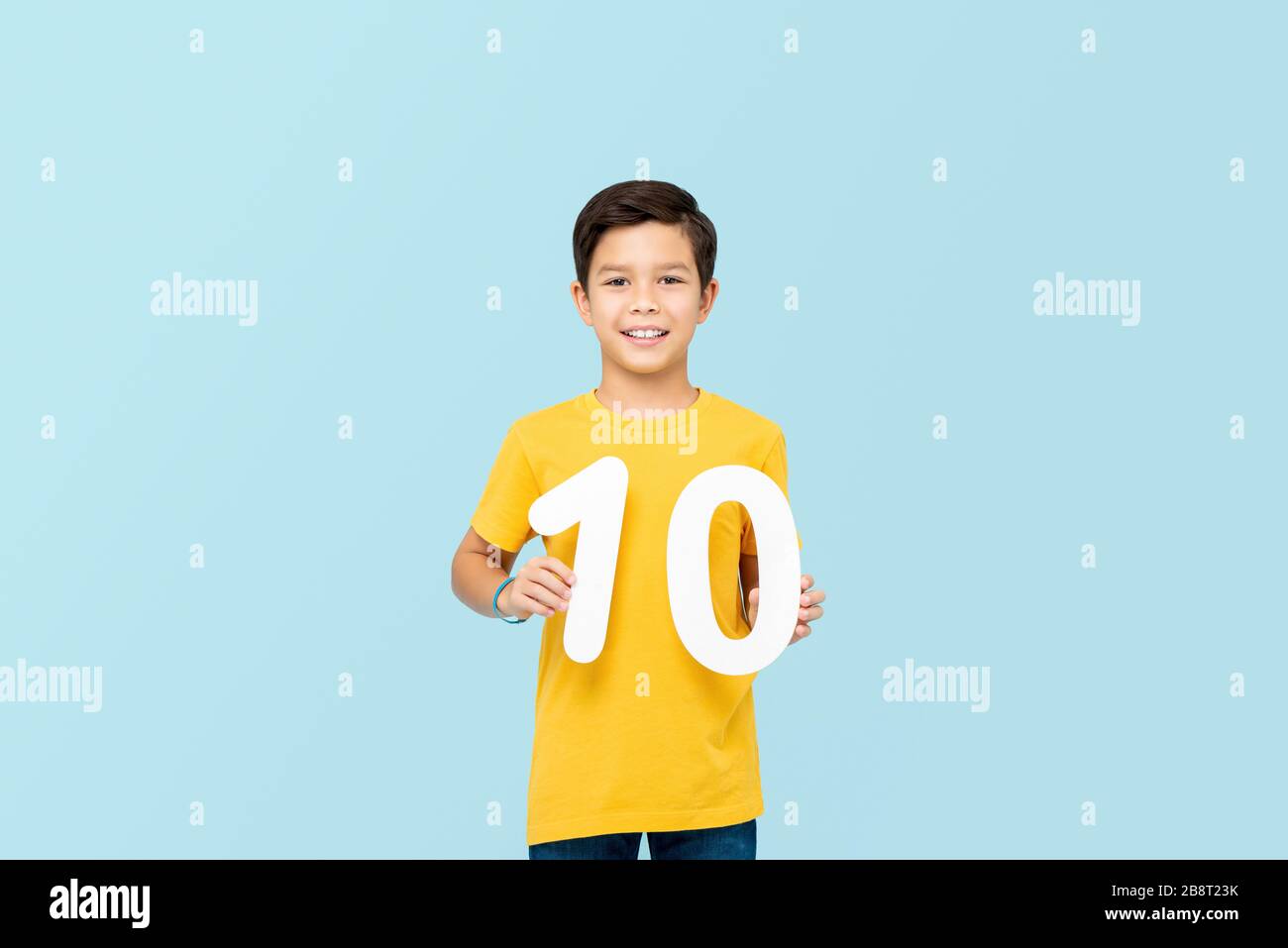 Guapo chico de 10 años de carrera mixta sonriendo y sosteniendo números aislados en el backround azul claro Foto de stock