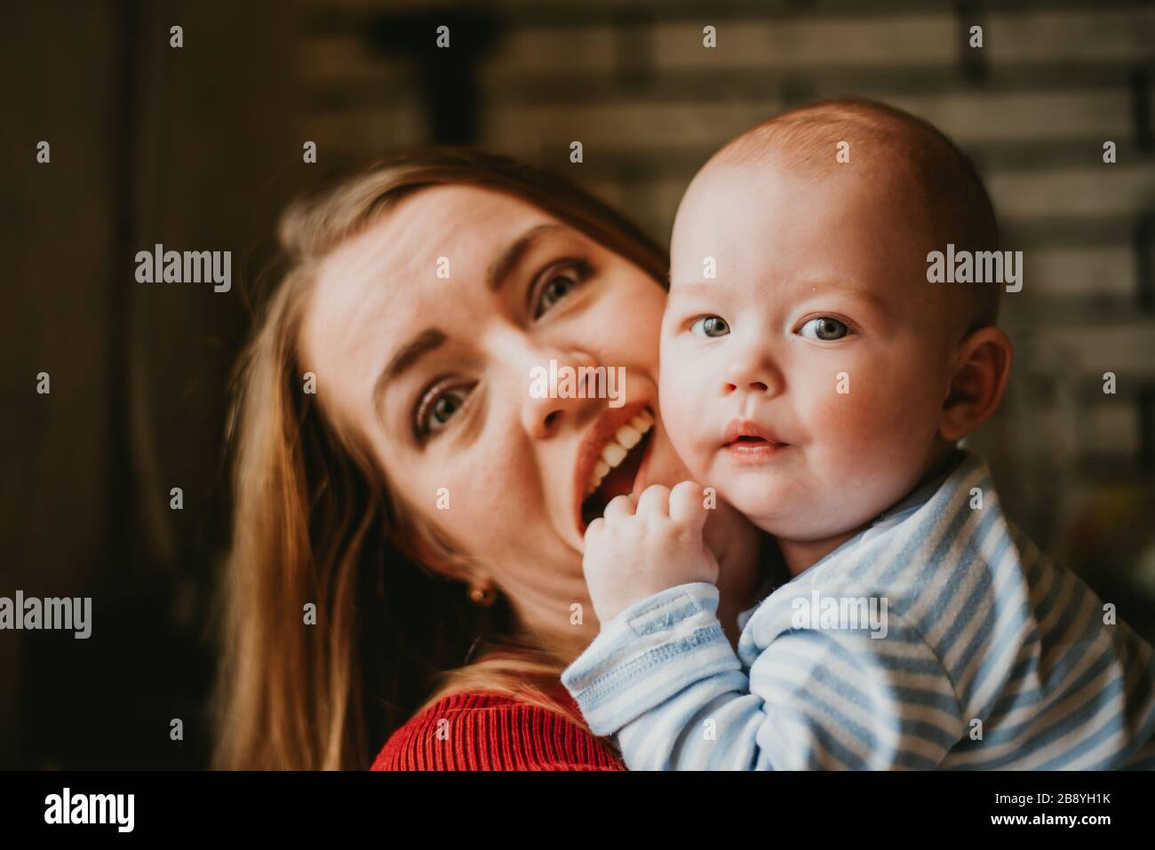 Una mamá sostiene a un bebé en sus brazos. La madre se jala a su hijo. Una mujer joven se divierte y se regocija con el niño. Una niña se embraga a un infant.Close para arriba. Foto de stock