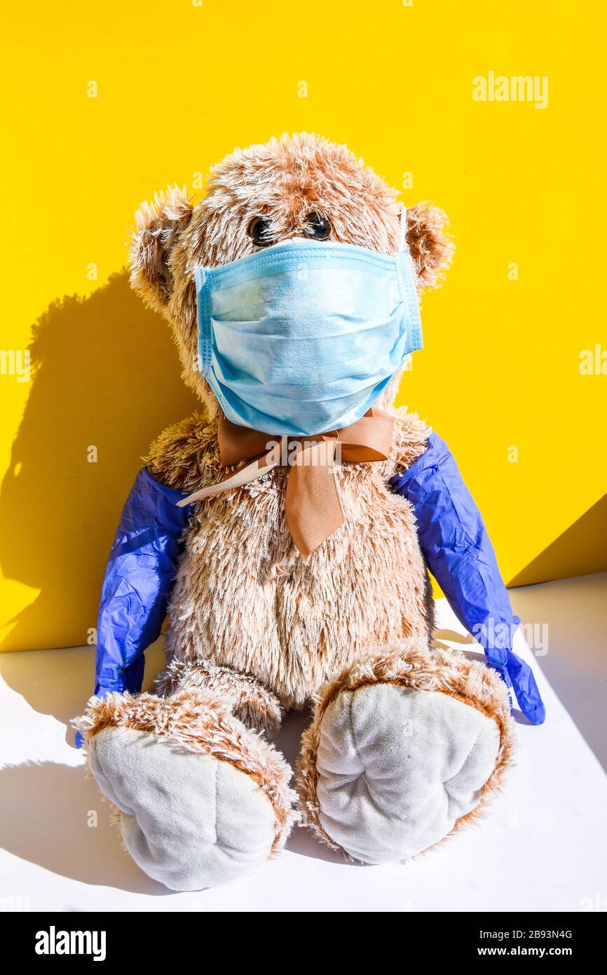 Coronavirus covid-19 y concepto de protección contra la contaminación. Muñeca de oso de peluche con máscara y guantes protectores sobre fondo amarillo, espacio de copia Foto de stock