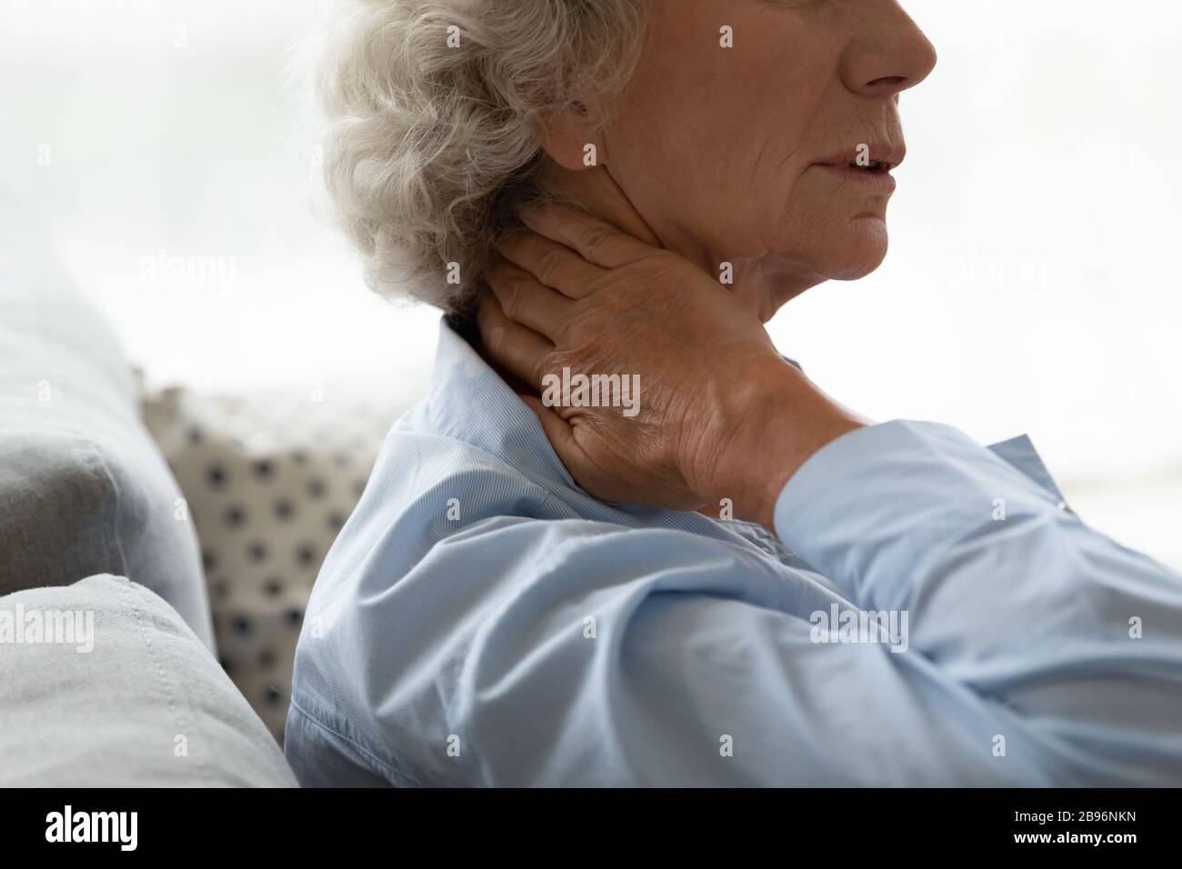 Una mujer anciana enferma toca el cuello y sufre de dolor Foto de stock