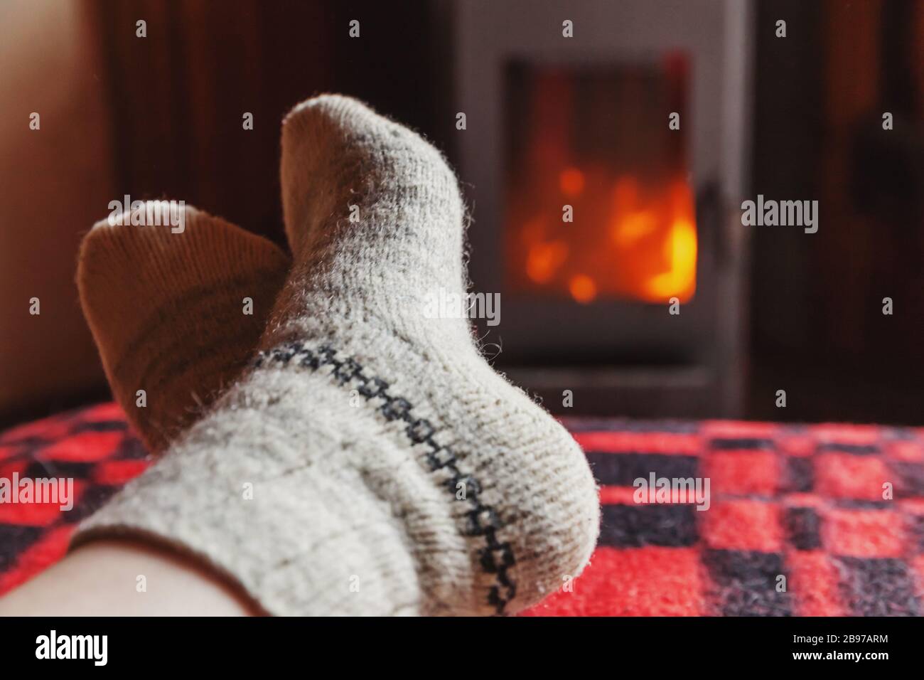 Pies piernas en ropa de invierno calcetines de lana en la chimenea de fondo. Mujer sentada en su casa en el invierno o el otoño tarde relajándose y calentando. El invierno y el frío concepto. La víspera de Navidad Hygge Foto de stock