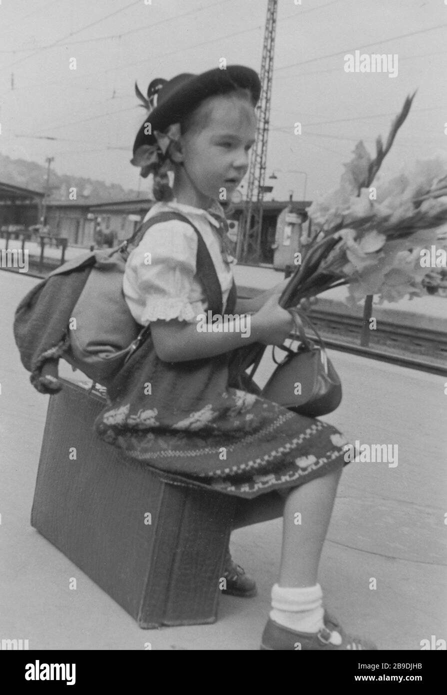 Una chica se sienta en una maleta en la estación y lleva un traje de punto. [traducción automática] Foto de stock
