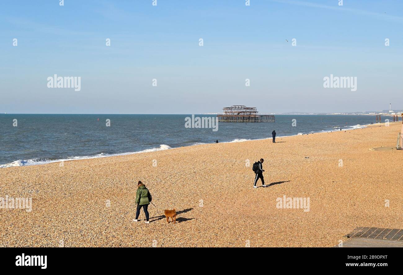 Brighton Reino Unido 24 de marzo de 2020 - la gente mantiene su distancia el uno del otro mientras que toman ejercicio en la playa de Brighton en una mañana soleada hermosa como las nuevas restricciones del gobierno vienen adentro durante la crisis pandémica del Coronavirus COVID-19 . Crédito: Simon Dack / Alamy Live News Foto de stock