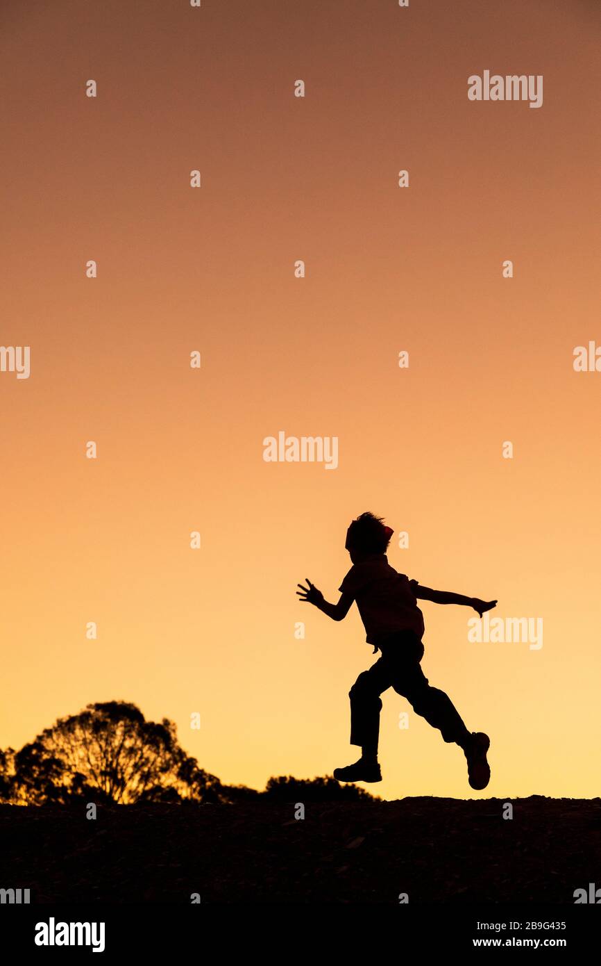 Silueta chico sin preocupaciones corriendo contra el cielo dorado de la puesta de sol Foto de stock