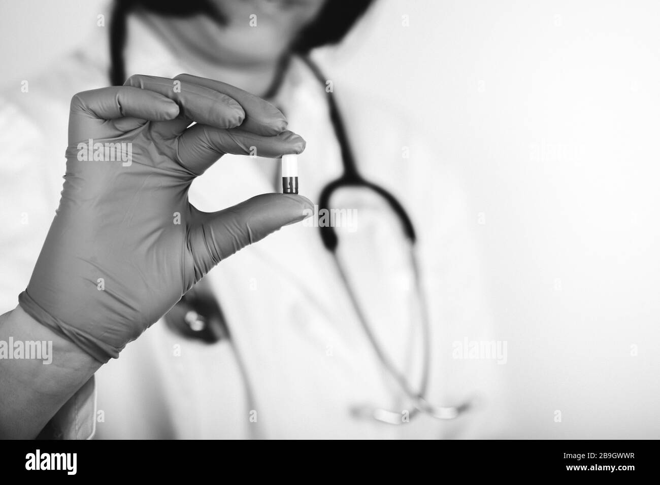Doctor en abrigo médico blanco y guantes estériles que sostienen una cápsula médica. Foto en blanco y negro. Foto de stock