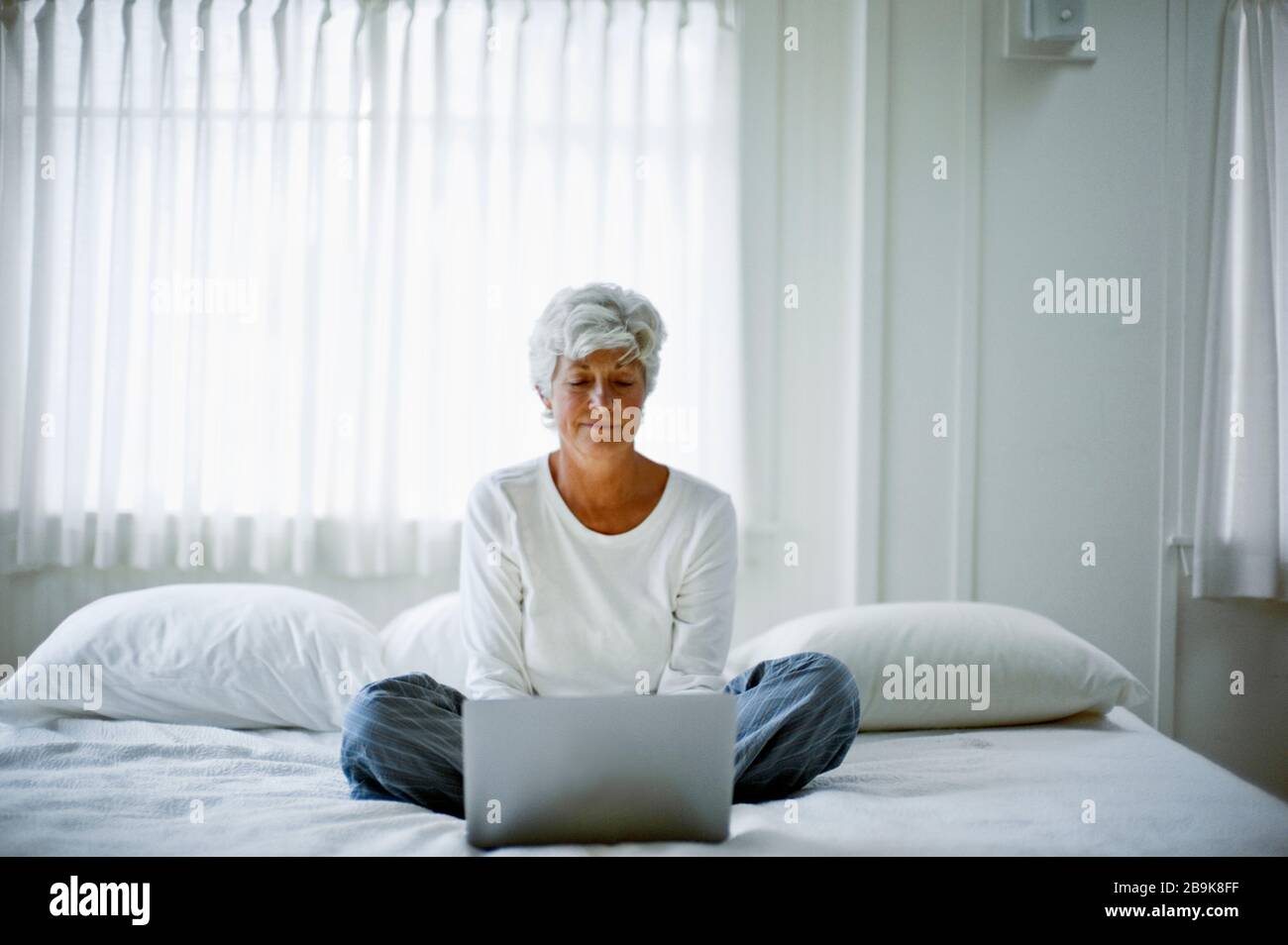 Una mujer madura en su pijama se sienta con piernas cruzadas en una cama y  mira hacia abajo a un portátil Fotografía de stock - Alamy