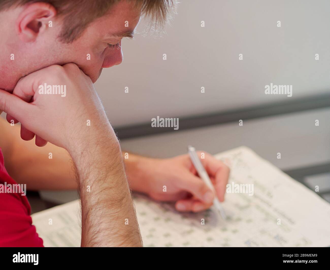 Primer plano de un hombre sosteniendo un lápiz que resuelve crucigramas usando una camisa roja en su tiempo libre. Foto de stock