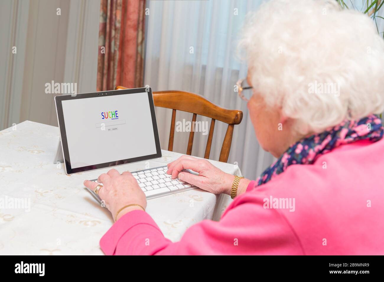 mujer de 80 años sentada sola en casa. Pertenece al grupo de riesgo de Covid 19. La mujer mayor escribe en el tablet PC contra el aislamiento con su f Foto de stock