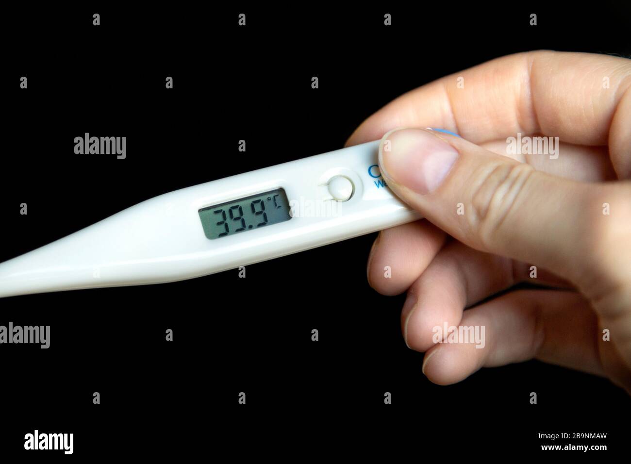 Mano sosteniendo un termómetro que muestra fiebre alta de 39.9 °C. Foto de stock