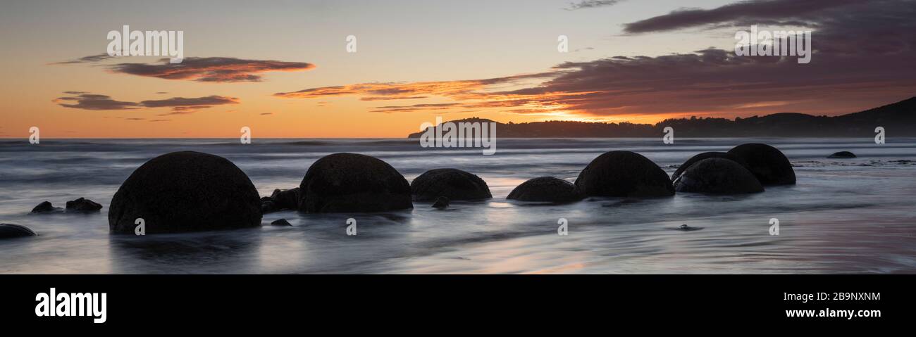 Moeraki Boulders al amanecer con un colorido cielo, Nueva Zelanda. Las rocas aparecen como siluetas rodeadas por el agua del mar en movimiento y el cielo adentro Foto de stock