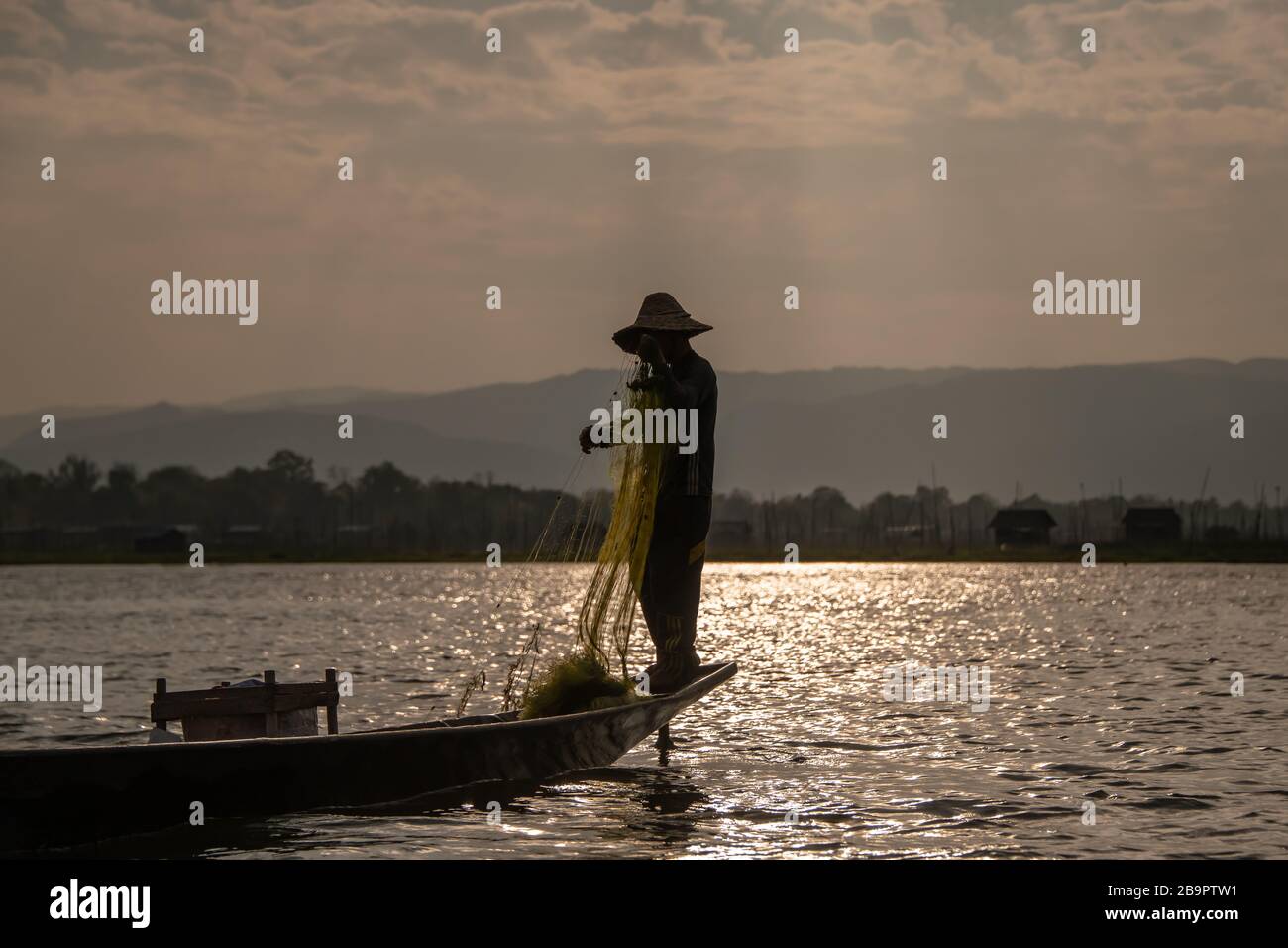 Lago Inle, Myanmar - 02 de febrero de 2020: Pescador tradicional de remo de tha con una red de yeso, iluminado por el sol de puesta. Foto de stock