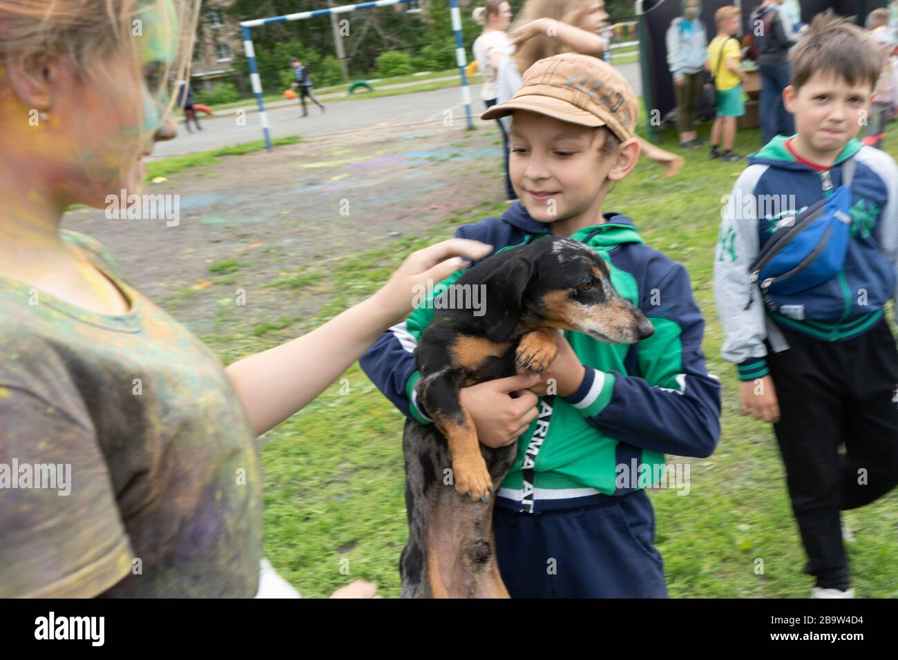 Región de Chelyabinsk, Rusia - JULIO de 2019. En la fiesta de los colores, los niños acarician al perro con sus manos. La cabeza del perro está manchada con pintura Foto de stock