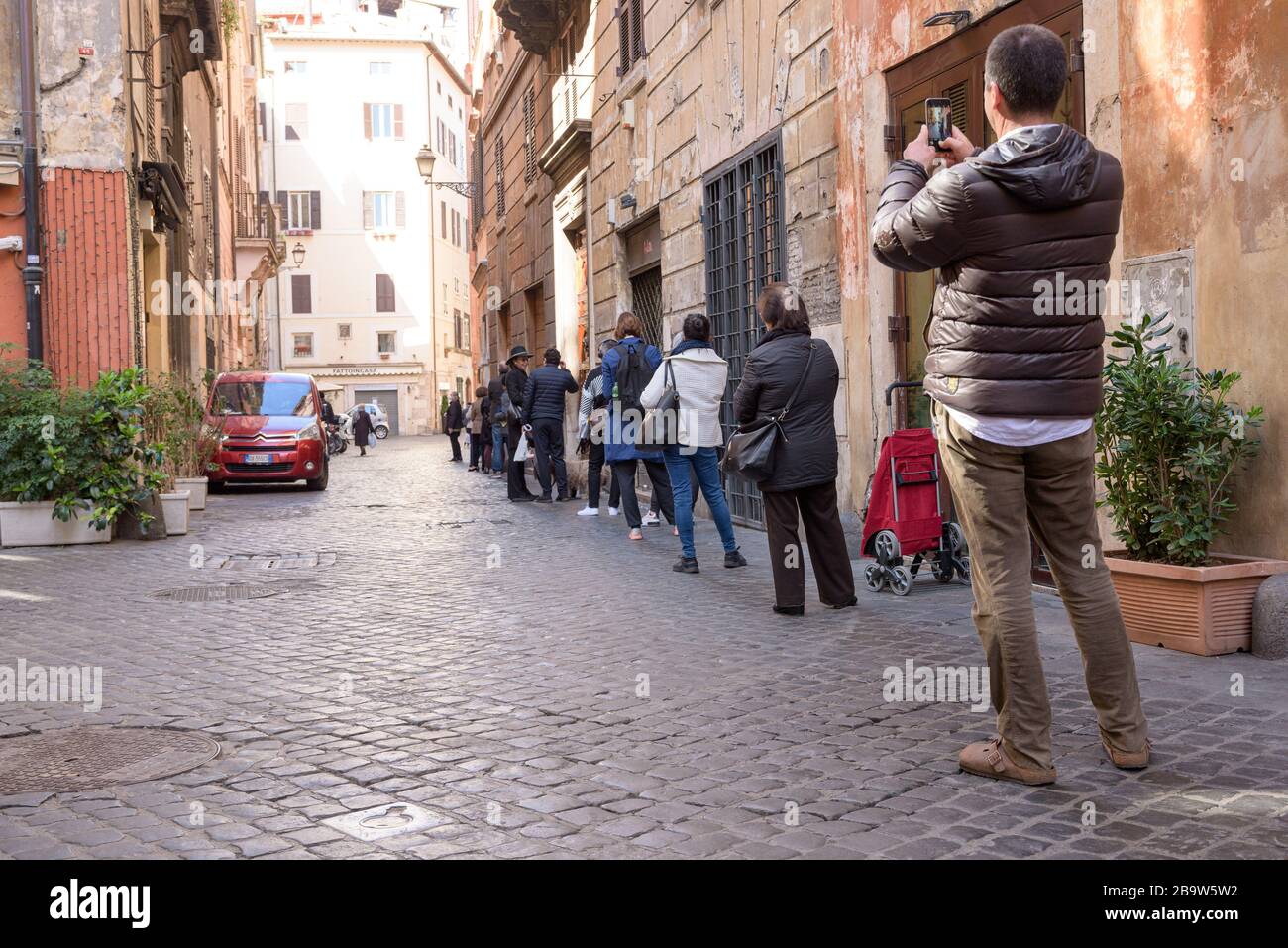 ROMA, ITALIA - 12 de marzo de 2020: Los clientes se alinean fuera de un supermercado local en el centro de Roma, Italia. Sólo unas pocas personas pueden entrar a la vez, y shal Foto de stock