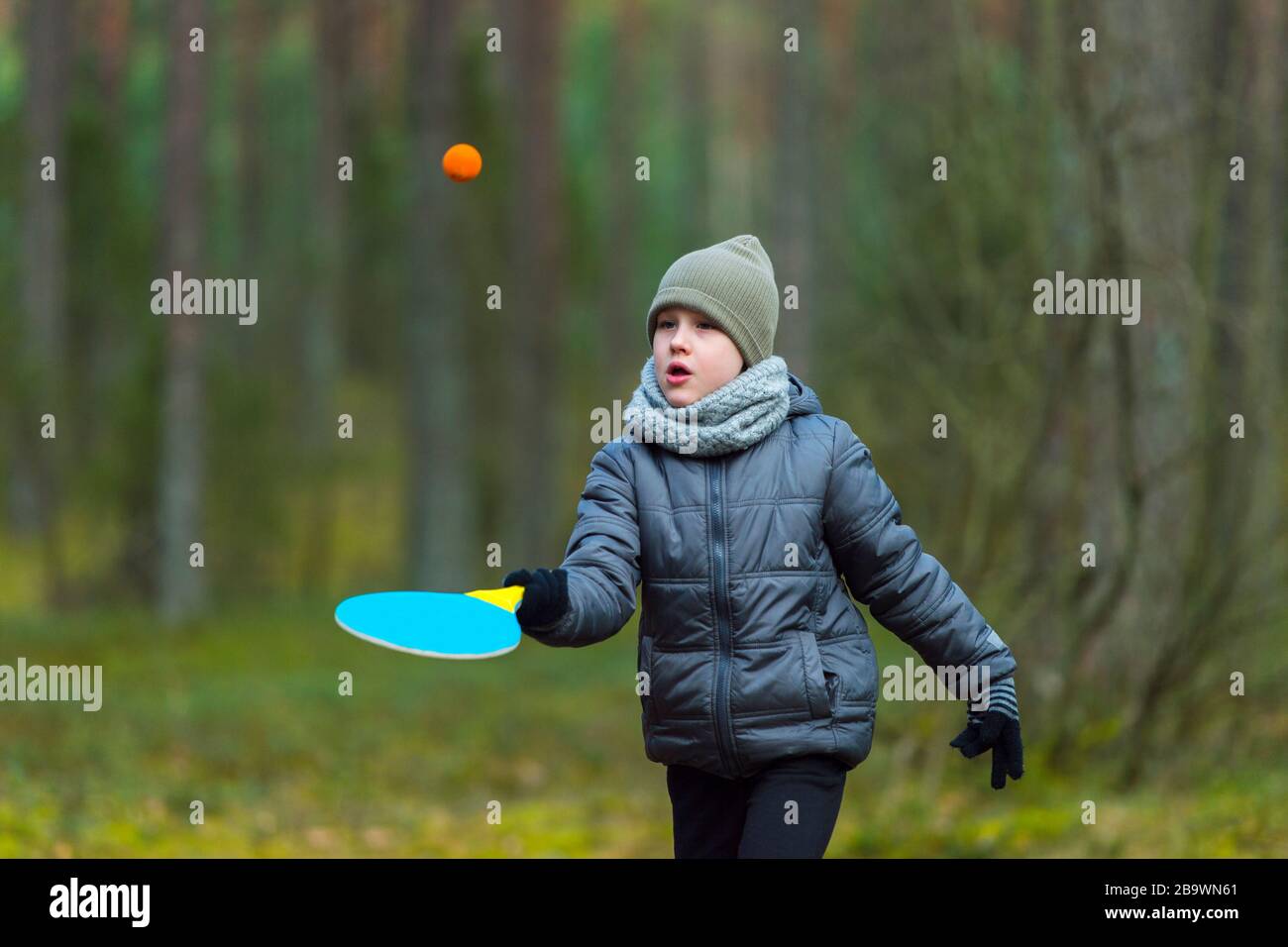 Un niño pequeño con una máscara debido al virus de la corona juega al tenis en el parque. Cuarentena de coronavirus Foto de stock