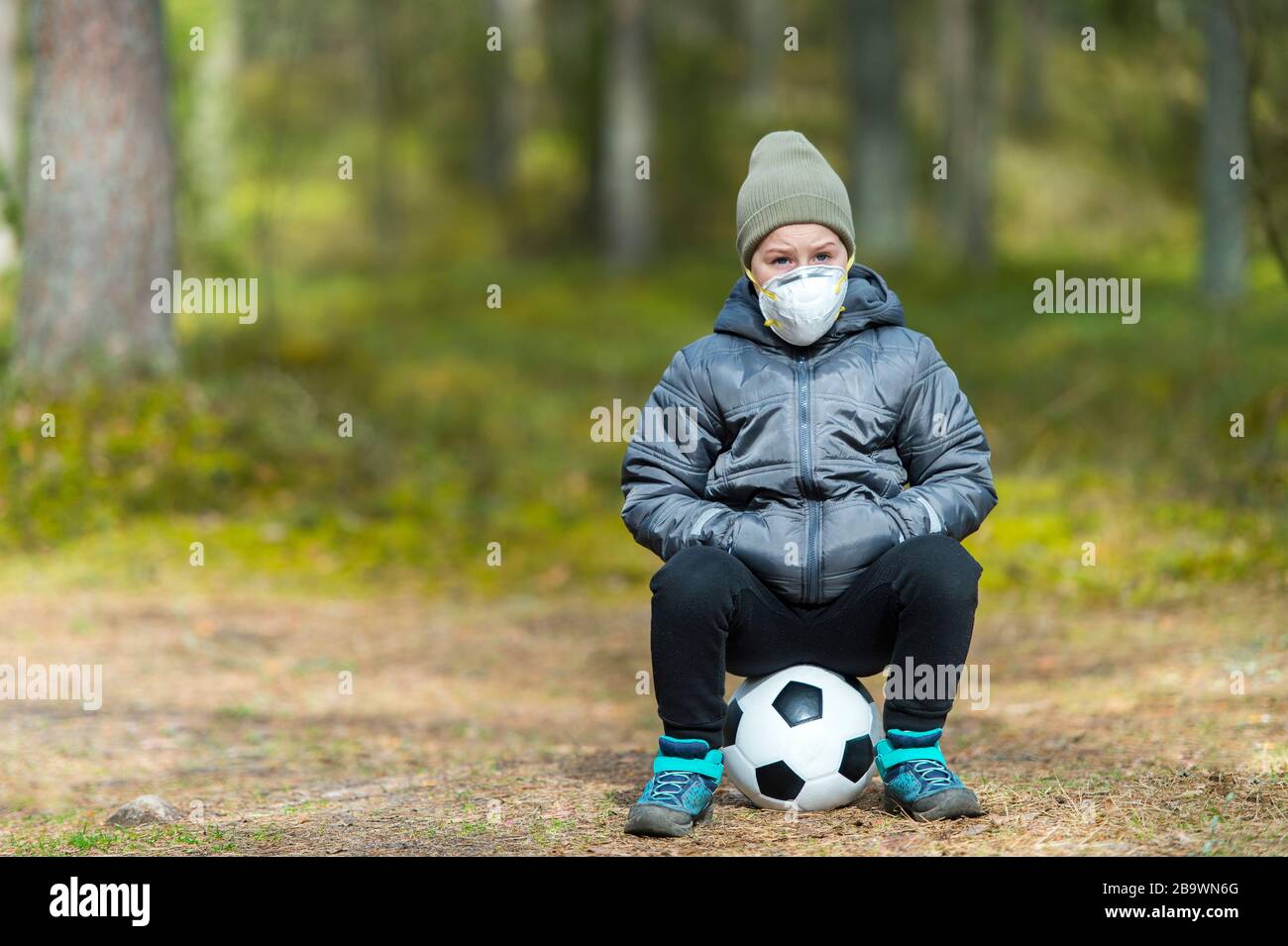 Niño pequeño con una máscara y una pelota de fútbol en el parque. Cuarentena del virus de la corona Foto de stock