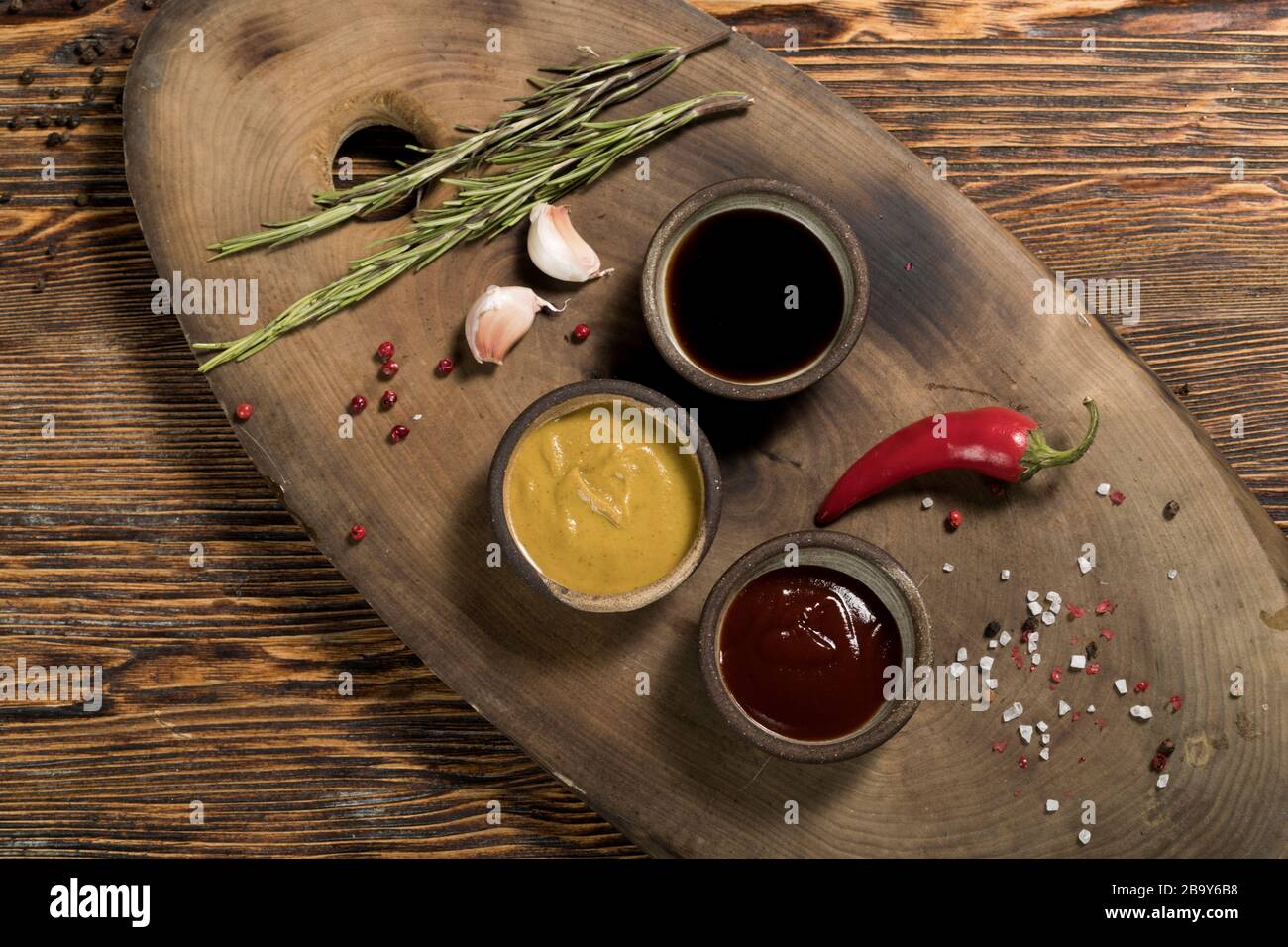 Ingredientes, ajo, romero, pimienta de Chile, salsa de tomate y soja, mostaza, especias, pimienta roja y negra, sal sobre un hermoso fondo de madera oscura, Foto de stock