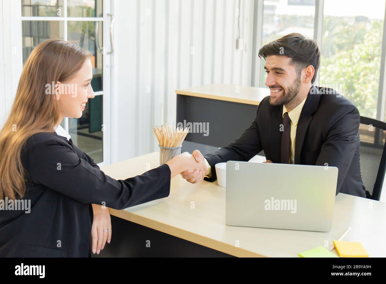 Retrato de un sonriente empresario europeo apretón de manos con su pareja empresarial femenina, dos personas exitosas se felicitan unos a otros agitando la mano Foto de stock