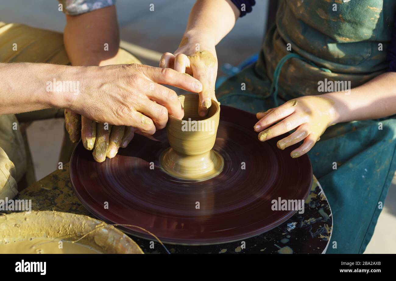 Las manos sobre una rueda de alfareros esculpen platos de arcilla amarilla. El maestro y el discípulo. Artesanía Foto de stock