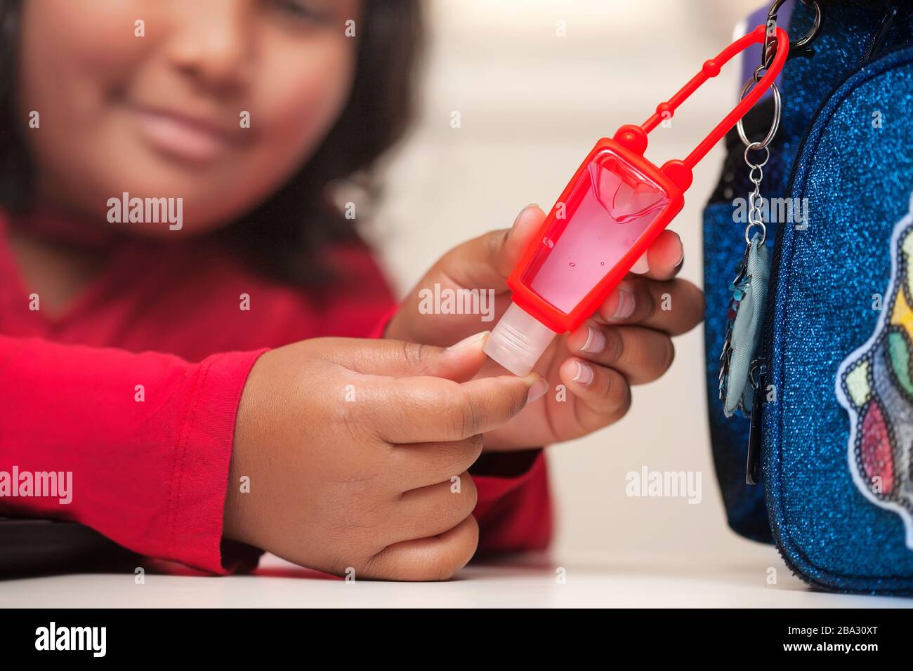 Un estudiante latino que llega a abrir un pequeño desinfectante de manos de gel a base de alcohol que está conectado a su mochila. Foto de stock