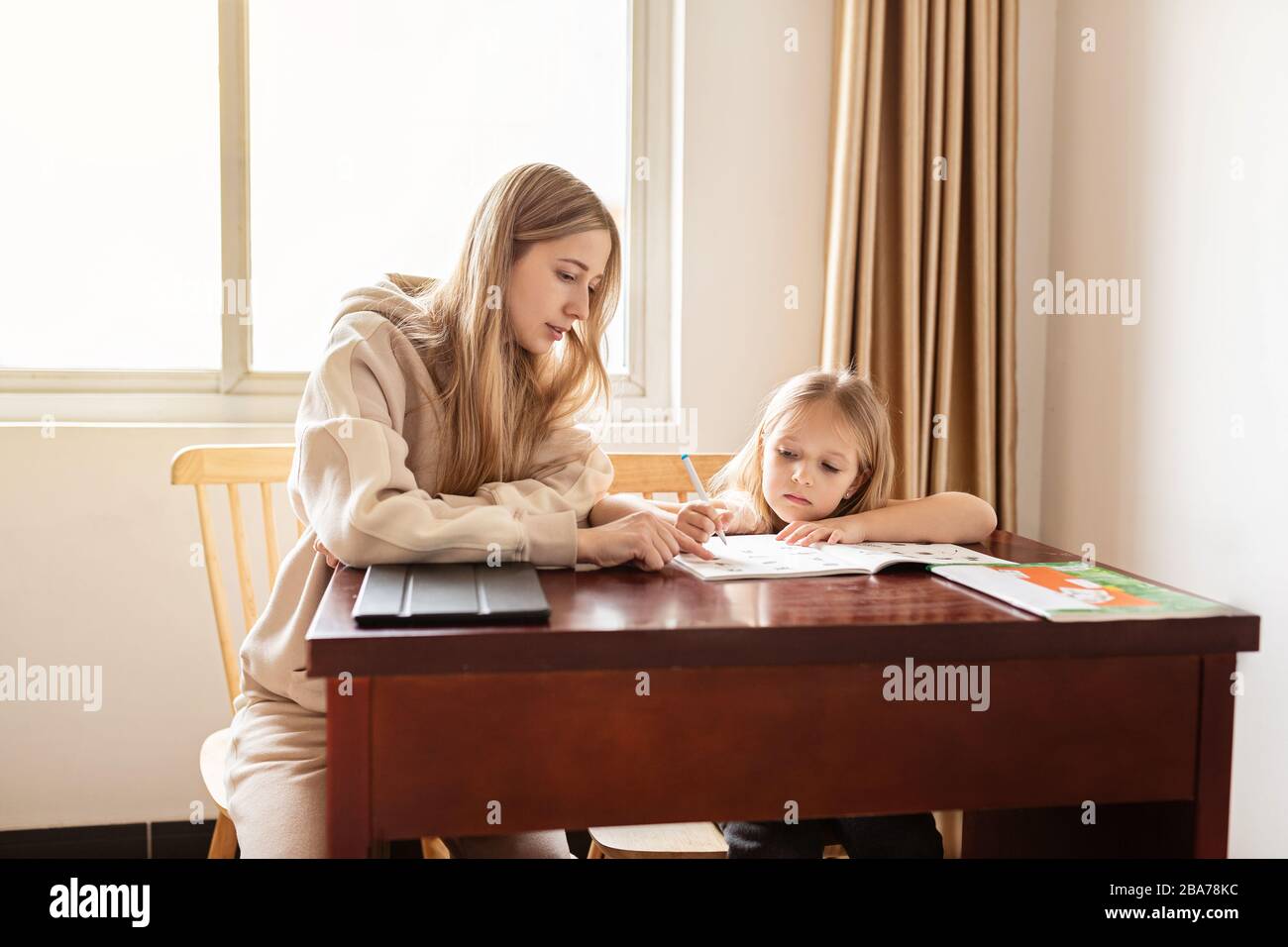 Madre ayudando a su hija a hacer la tarea escolar en casa. Aprendizaje en casa, aprendizaje en línea, autocuarentena, escolarización en casa y concepto de COVID-19 Foto de stock