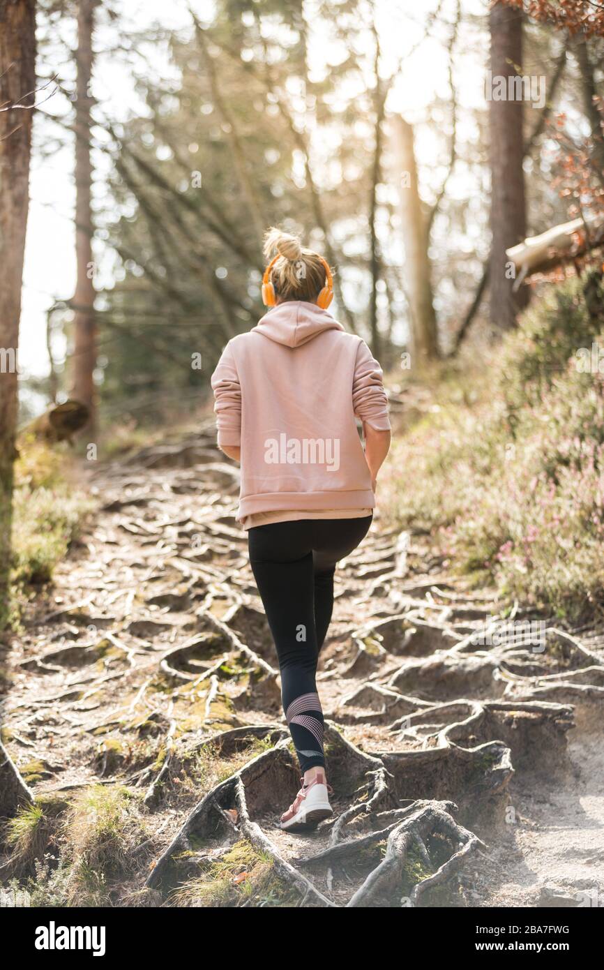 Vista trasera de una mujer deportiva activa que escucha la música mientras corre en otoño bosque de otoño. Entrenamiento de corredor femenino al aire libre. Imagen de estilo de vida saludable Foto de stock