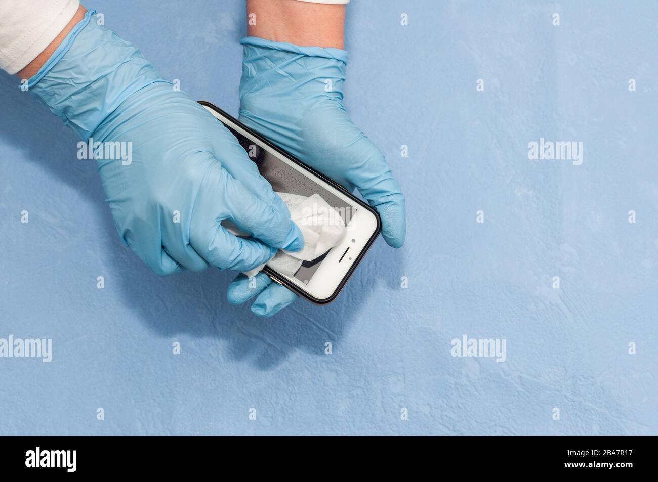 Desinfectando un teléfono móvil, una mujer aplica un spray antiséptico a base de alcohol a un grifo para prevenir la propagación del virus Foto de stock