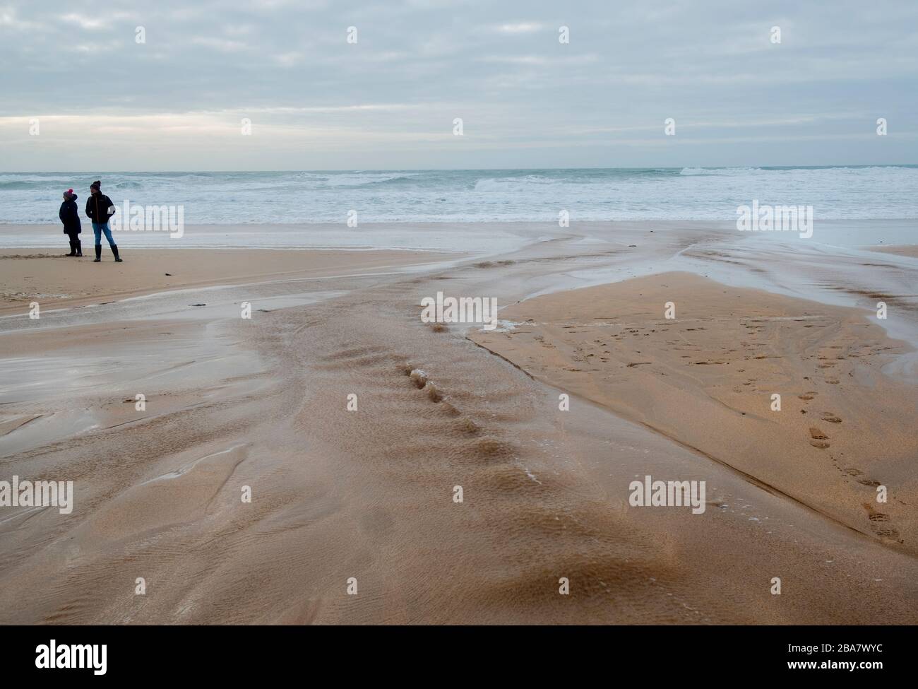 Constantine Bay, una hermosa playa de arena cerca de Ttevose en Cornwall, en un día otoñal con dos personas disfrutando del aire fresco caminando a lo largo de la marea baja Foto de stock
