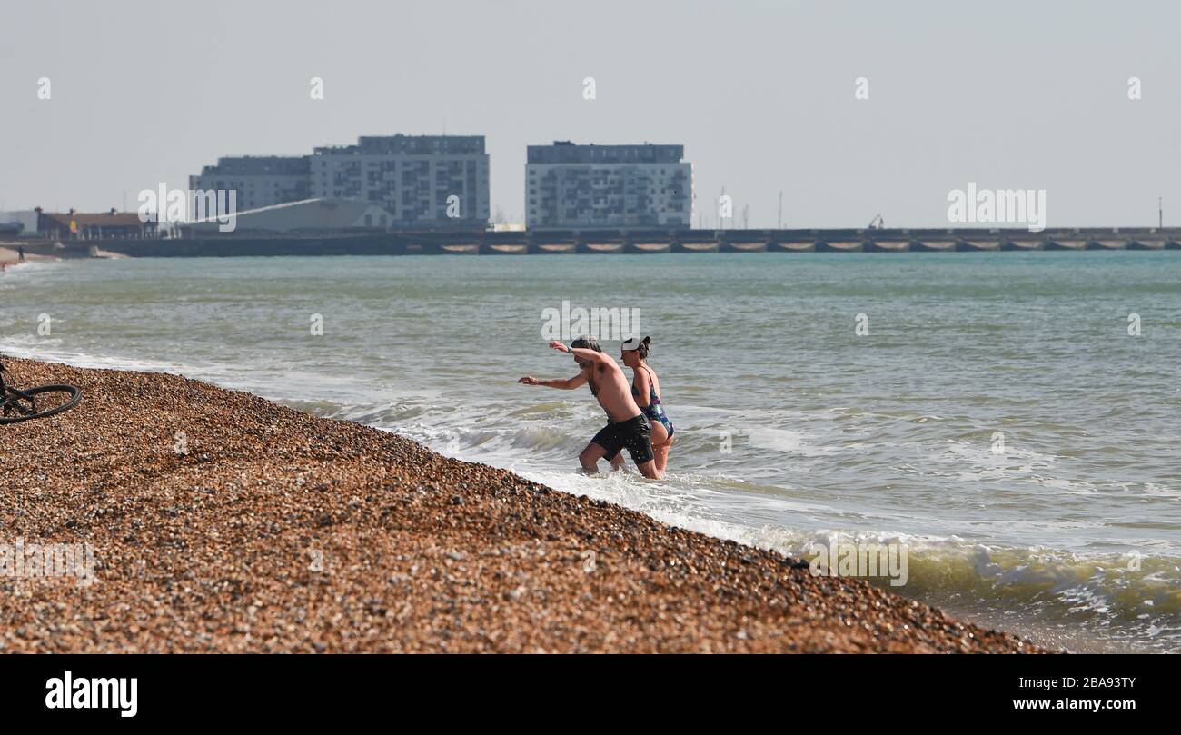 Brighton Reino Unido 26 de marzo de 2020 - los nadadores disfrutan de un chapuzón en el mar frente a la playa de Brighton en el día tres de los gobiernos de bloquear las restricciones durante la crisis pandémica COVID-19 de Coronavirus . Crédito: Simon Dack / Noticias en vivo de Alamy Foto de stock