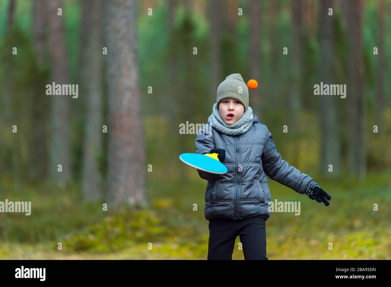 Un niño pequeño con una máscara debido al virus de la corona juega al tenis en el parque. Cuarentena de coronavirus Foto de stock