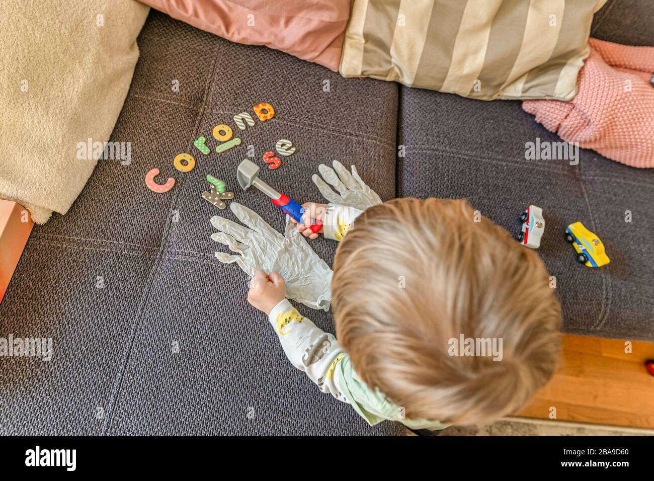 Letras escritas Corona KRise en alemán palabras con un niño pequeño viendo los guantes de desinfección mientras interrumpe su juego. Foto de stock