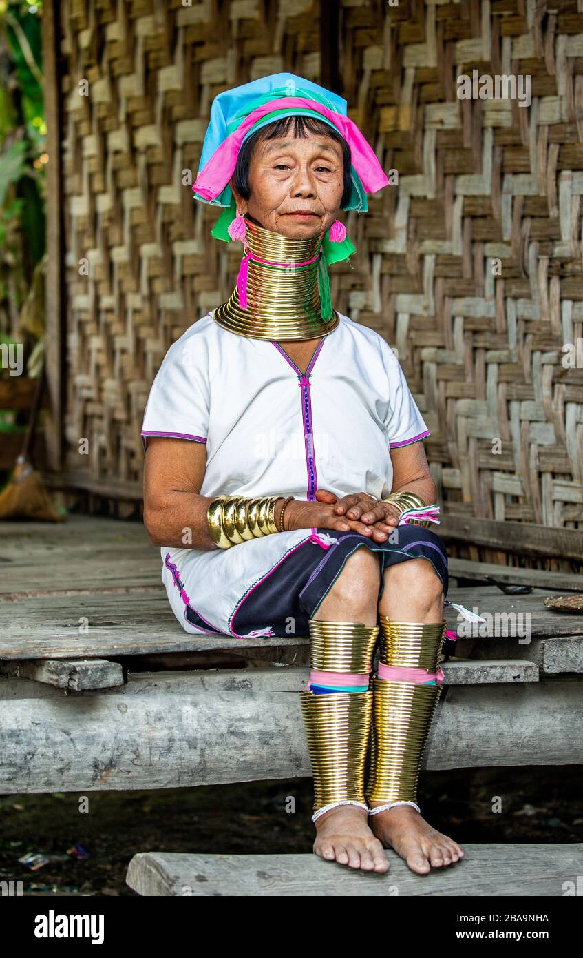 Mujer Padaung de edad con vestido tradicional y con anillos de metal  alrededor de su cuello, brazos y piernas está sentada en una escalera en  una casa de pueblo Fotografía de stock -