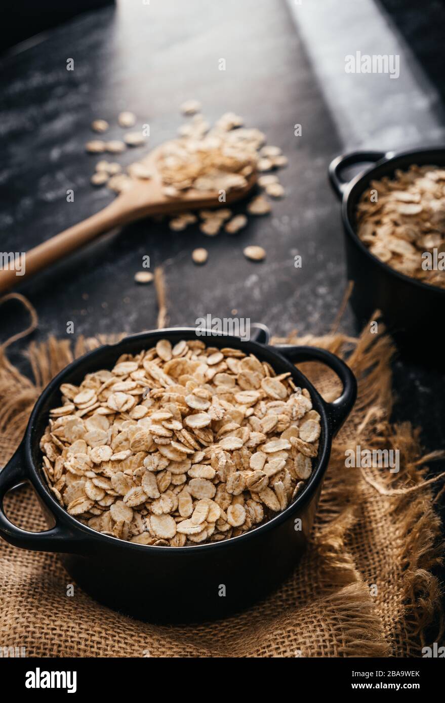 Vista superior de dos cuencos negros y cuchara con avena cruda sobre fondo negro. Desayuno con fibras para una dieta equilibrada. Foto de avena Foto de stock