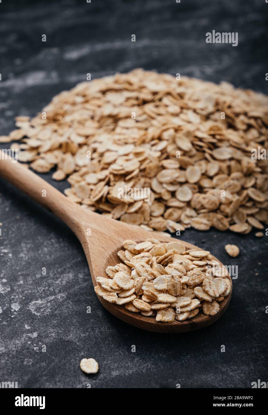 Cuchara llena de hojuelas de avena sobre fondo negro. Foto de stock