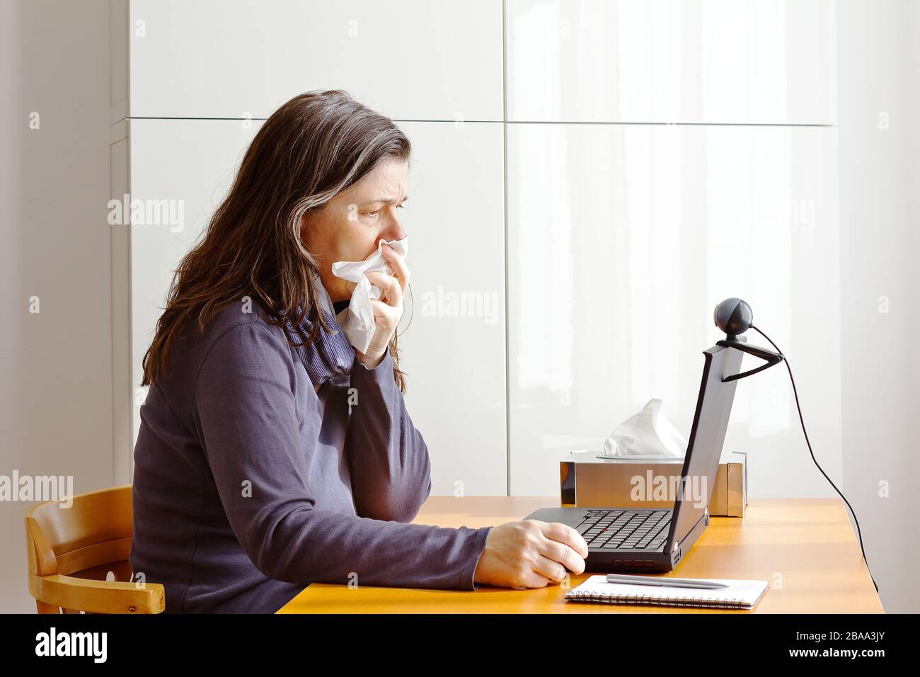 Línea directa del virus de la corona: Mujer con tos llamando a su médico en un ordenador portátil a través de enlace de vídeo. Foto de stock